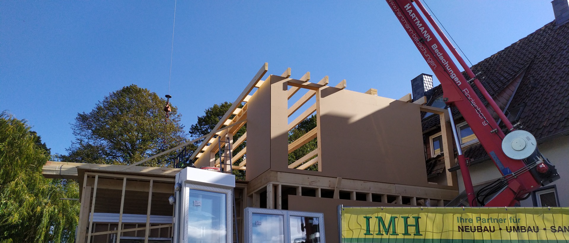 Wohnraumerweiterung im Bau: Holzrahmenkonstruktion eines Hausanbaus wird per Kran montiert, während Dach- und Wandmodule präzise eingesetzt werden.