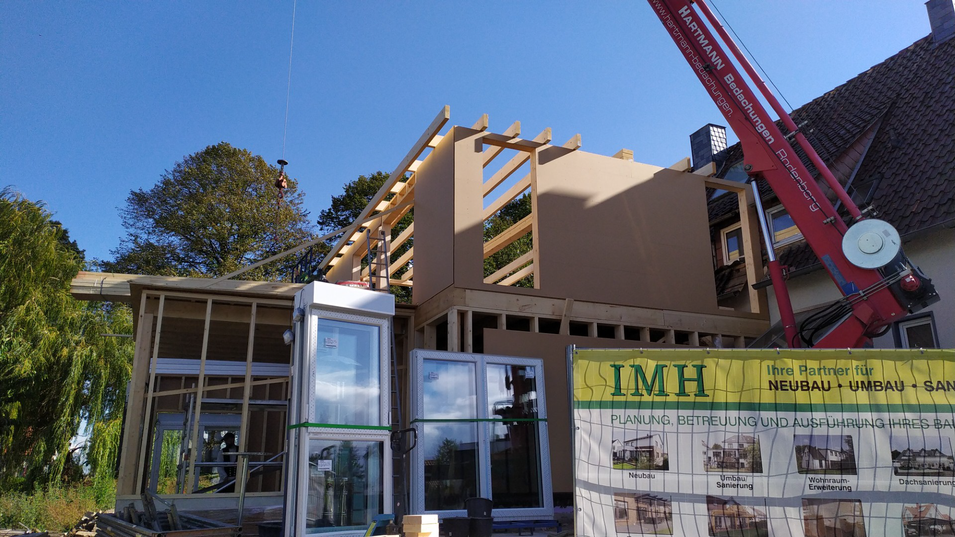 Baustelle mit Holzrahmenbau, Kran hebt Bauteile, moderne Erweiterung entsteht, kreative Ideen mit Holz für nachhaltiges Bauen und Architektur
